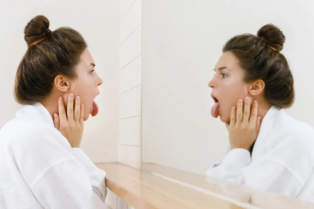 Woman looking at her tongue in a mirror. Knowing that her tongue and her oral health are related